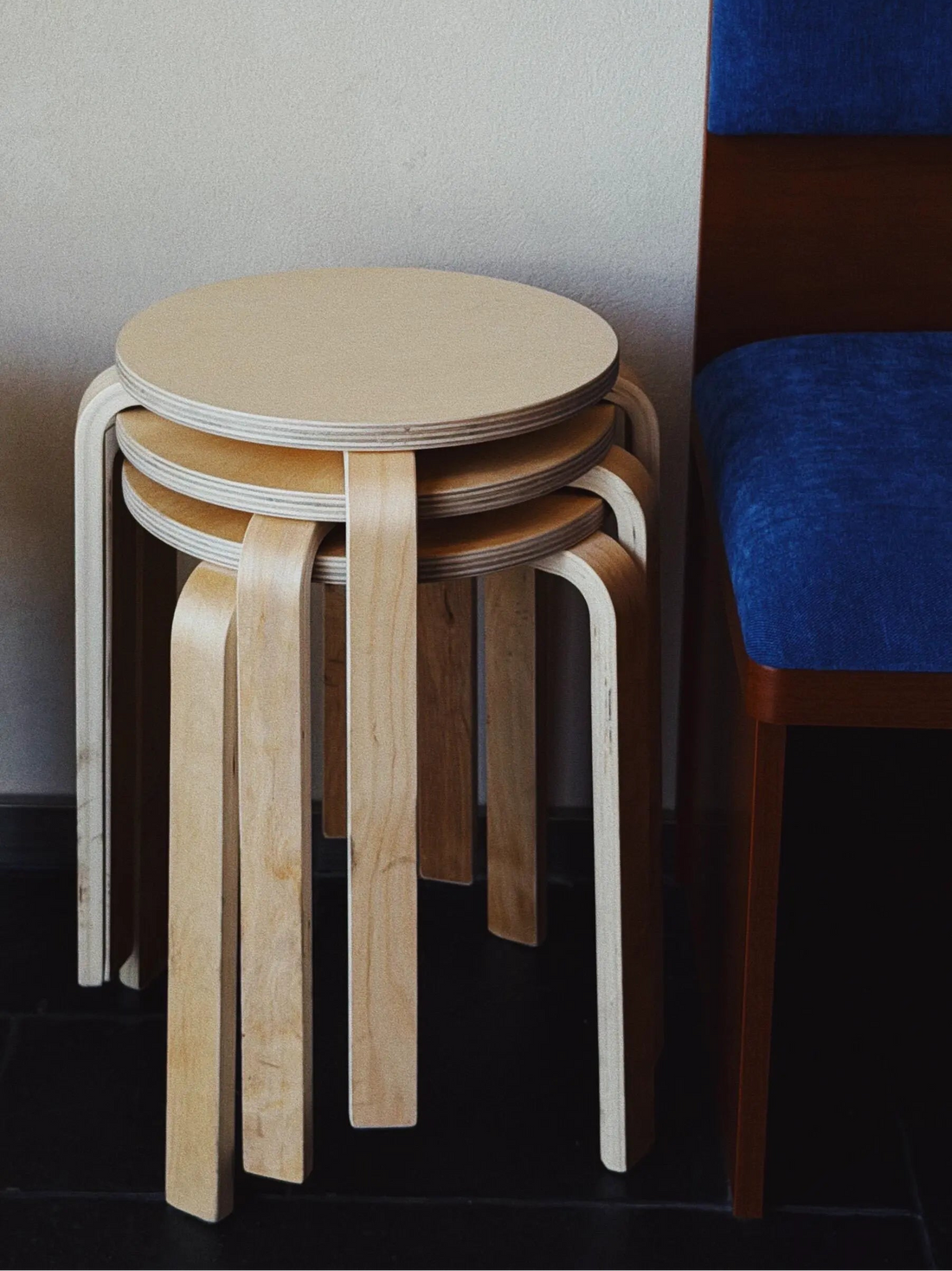 Stack of wooden stools against a neutral wall with a blue cushioned chair.